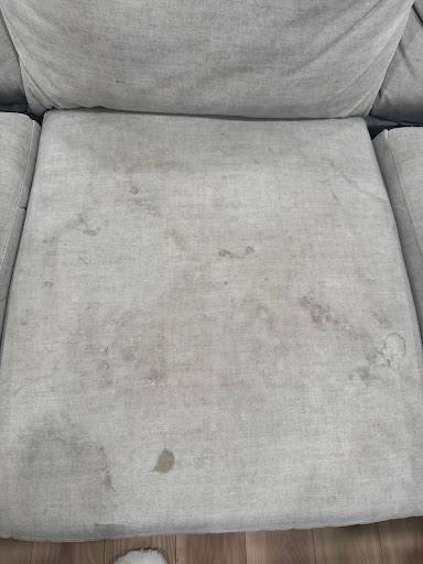 A light grey fabric sofa seat marked with dark stains, before cleaning
