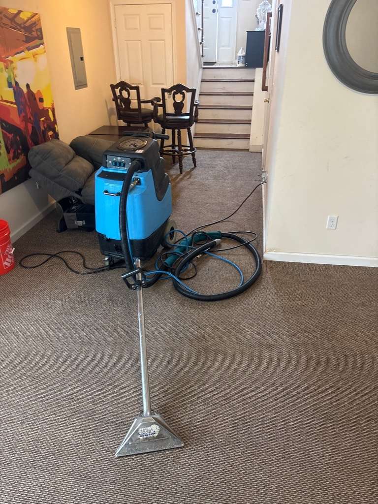 A portable extraction machine standing on carpet in a living room, its hose and wand run out across the floor