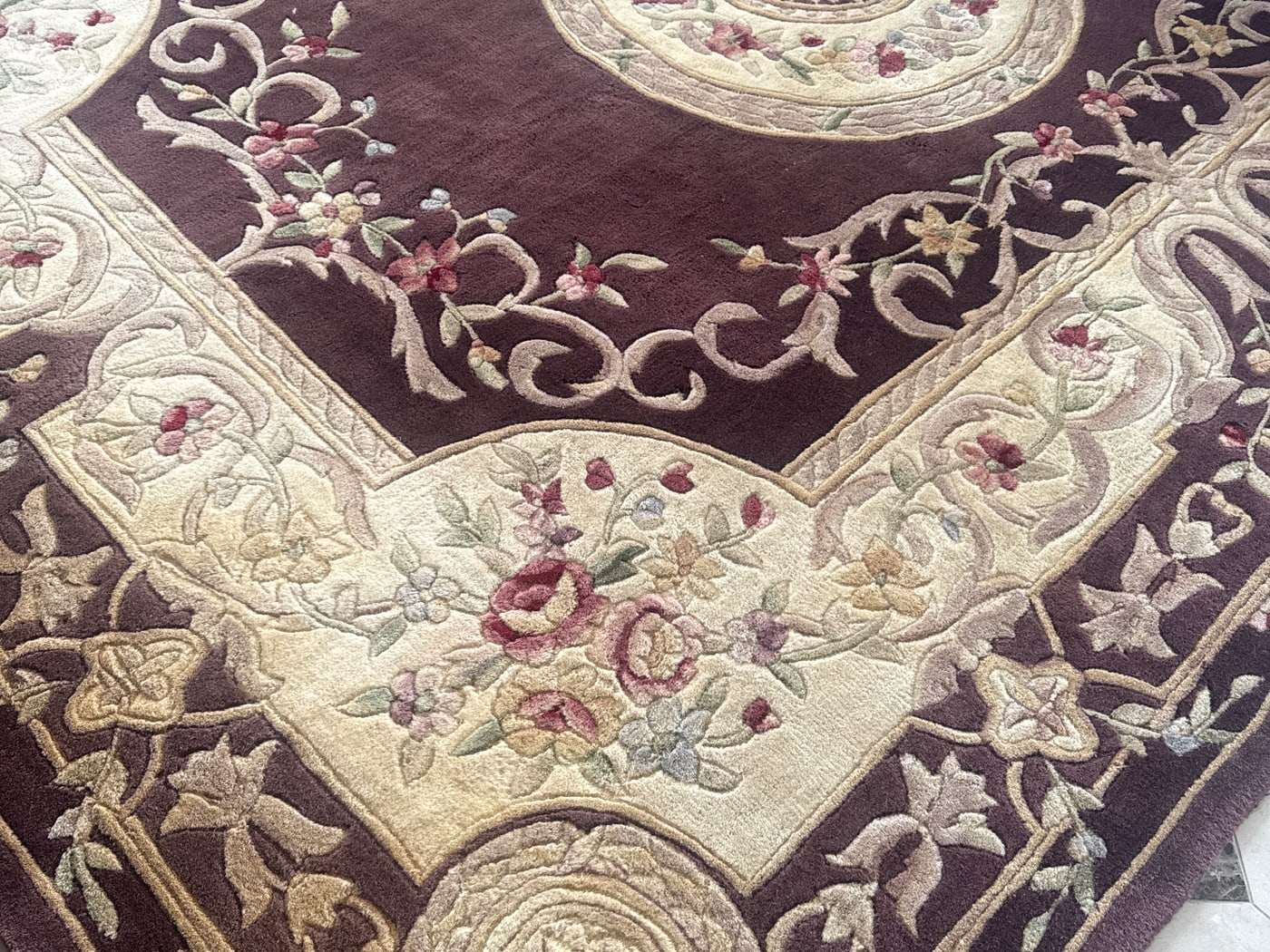 An ornate burgundy and cream wool rug on a tile floor after cleaning