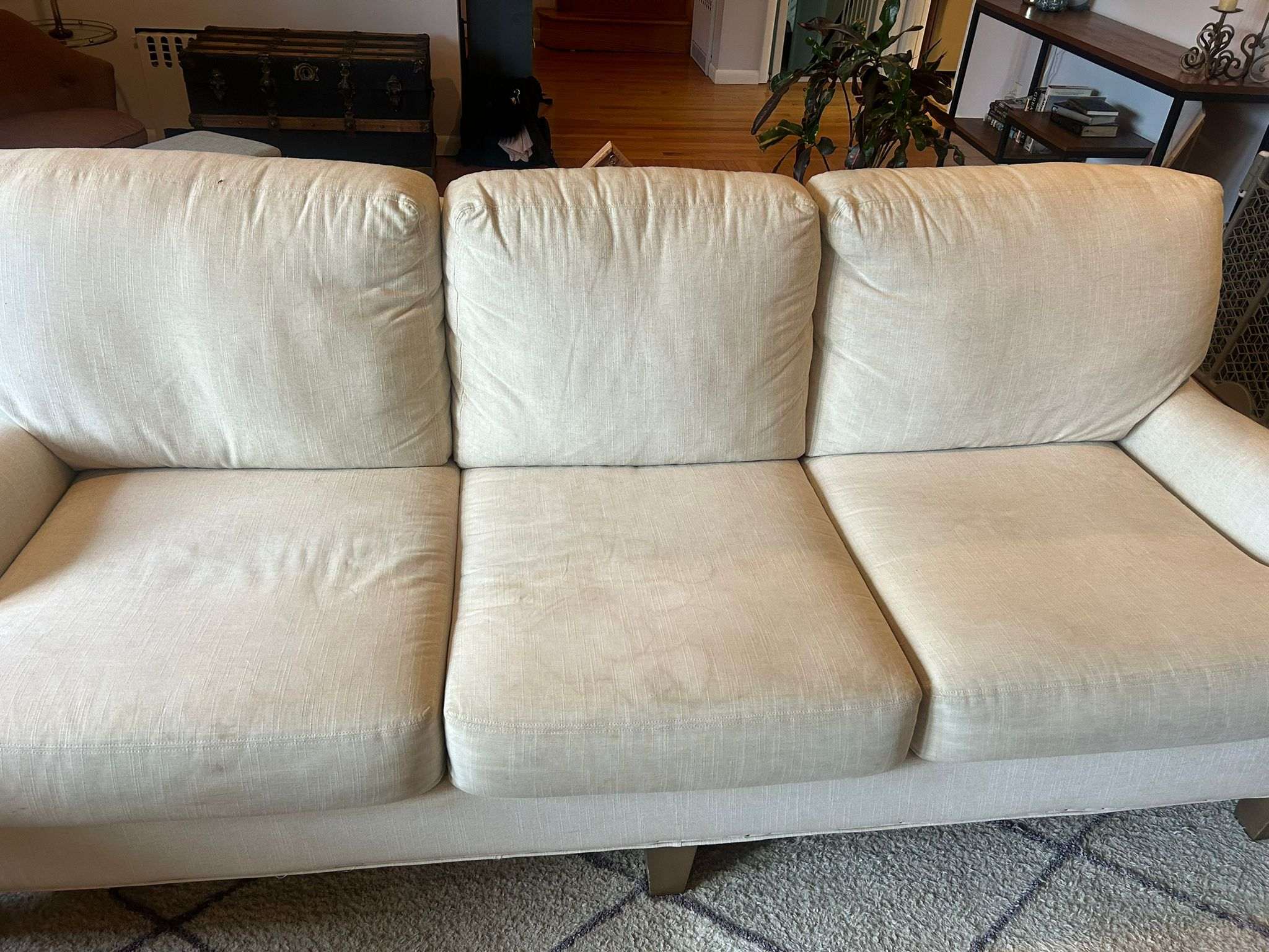 A cream fabric three-seat sofa in a living room, the seat cushions still carrying some shading after cleaning