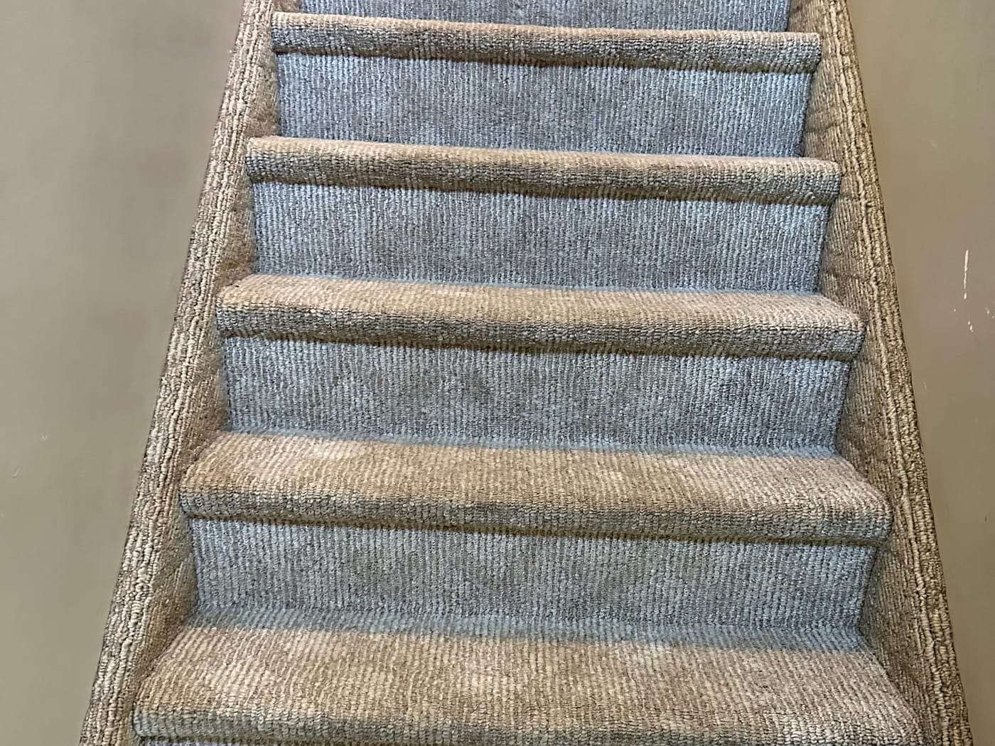 A flight of carpeted stairs after cleaning, oatmeal and blue-grey banding running up the treads