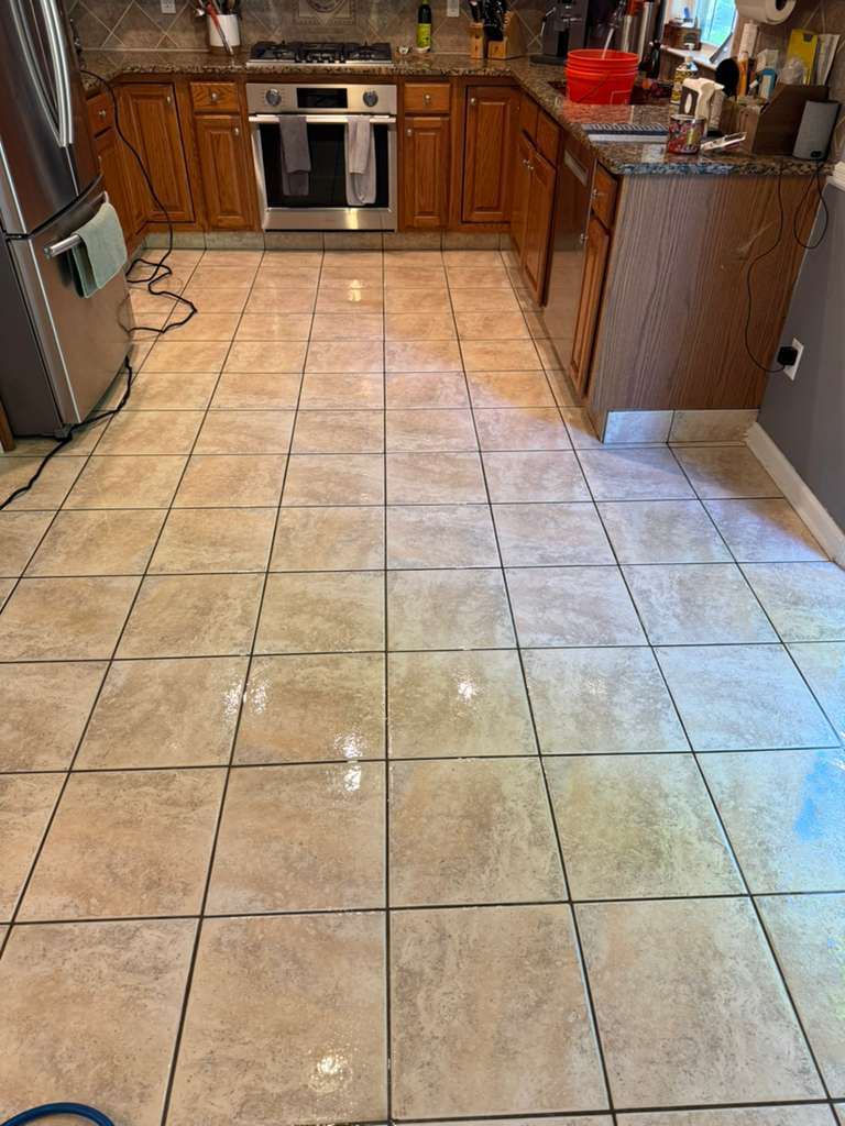 A kitchen tile floor after cleaning, the glaze reflecting the window and the grout joints even across the run