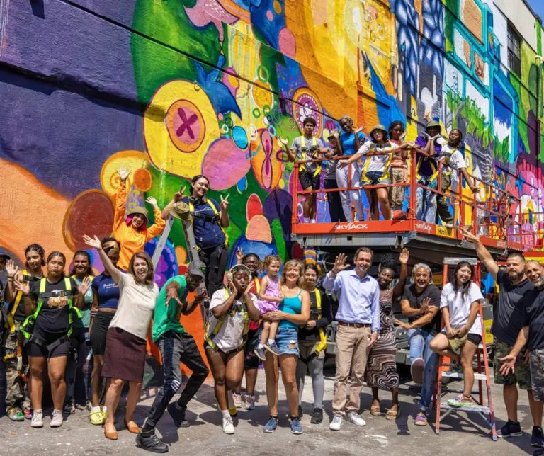 Vibrant public mural with community members gathered in front, highlighting Jersey City’s commitment to public art and cultural expression through the Mural Arts Program.